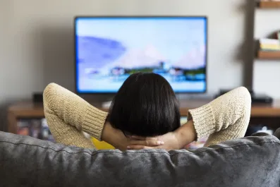 Mulher vendo TV sentada no sofá com a mão no pescoço