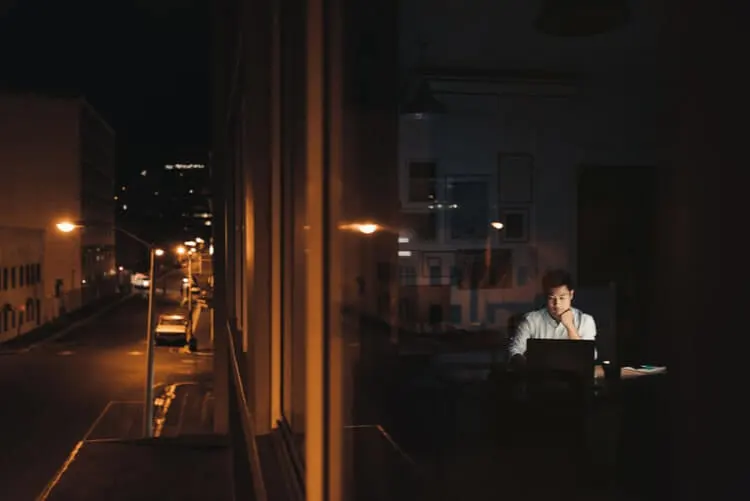 Homem trabalhando à noite na frente de um computador, com as luzes apagadas