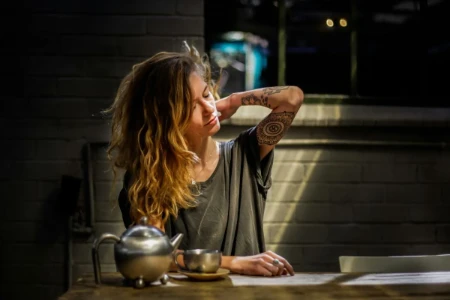Mulher jovem com dor nas costas segurando o pescoço e ombro, com expressão de desconforto.