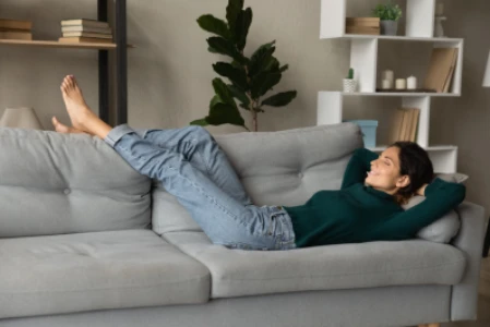 Mulher relaxando deitada no sofá, com as pernas elevadas, apoiadas no encosto.