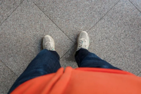 Detalhe de pés no cão, calçados com tênis. A pessoa também veste calça jeans e blusa laranja (a foto foi tirada de cima para baixo), pela própria pessoa.