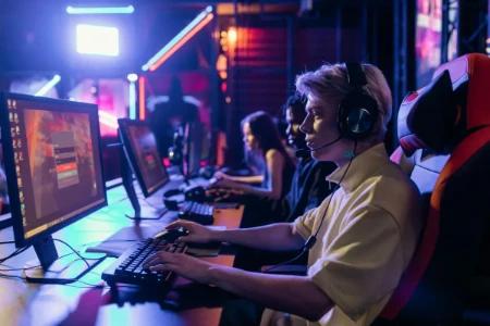 Jovem gamer utilizando um setup de computador ergonômico com monitor, teclado e mouse, fones de ouvido e cadeira gamer confortável, em um ambiente de eSports, destacando a importância da postura correta e prevenção de dores para jogadores.