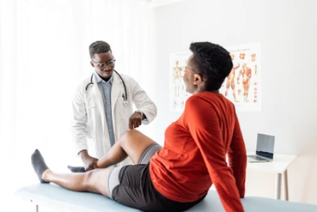 Mulher sentada na maca, com um joelho flexionado sendo avaliado por um médico.