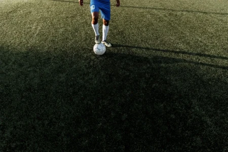 A imagem de um jogador de futebol parado com a bola, representando a necessidade de cuidados para prevenir lesões e manter a saúde para a prática do esporte.