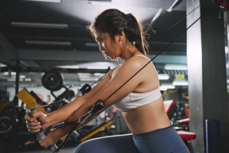 Mulher focada, fazendo exercício cruzado para músculo peitoral em pulley, na academia.