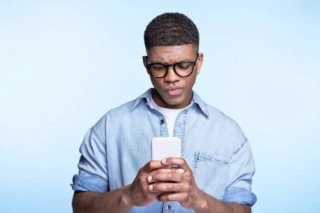 Homem com expressão confusa, segurando o celular com as duas mãos.