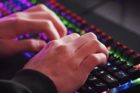 Detalhe de mãos de um jovem jogando em ambiente cheio de luzes neon, em PCs gamer.