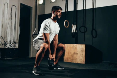 Homem em estúdio de crossfit faz agachamento segurando kettlebell