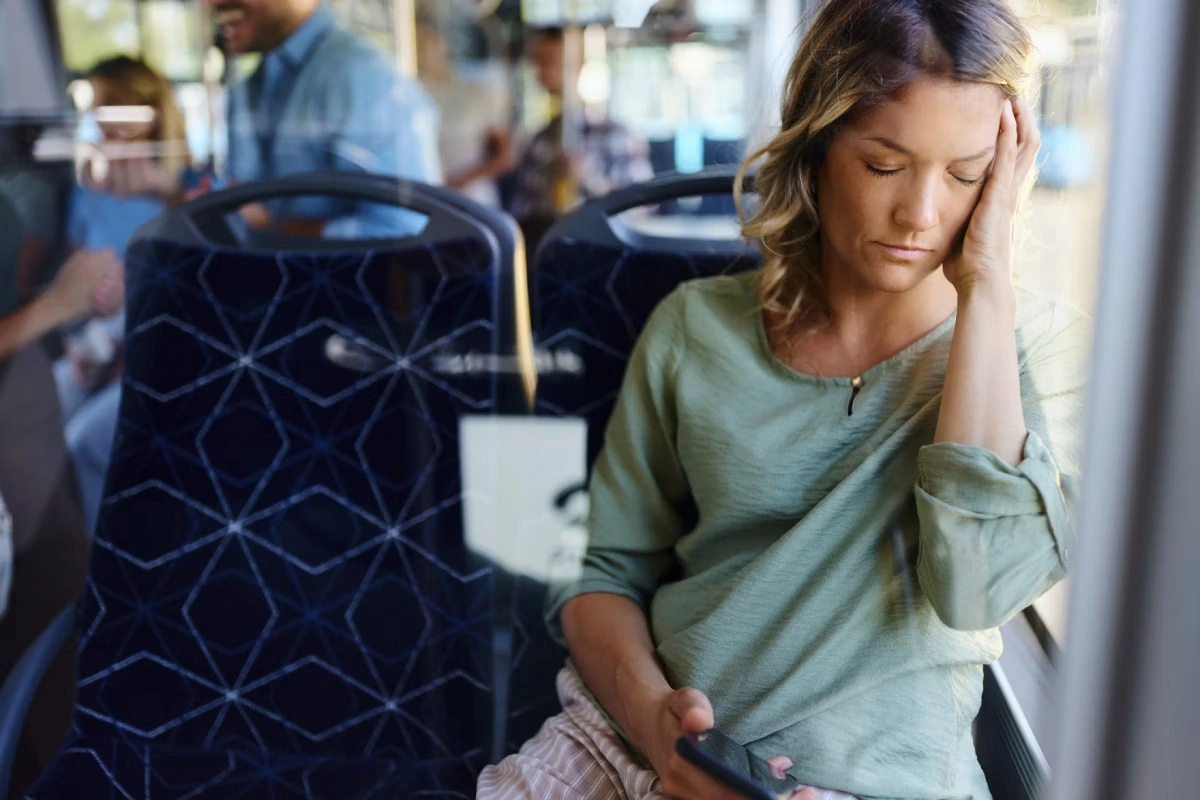Mulher sentada no ônibus, com mão apoiando cabeça que está encostada na janela.