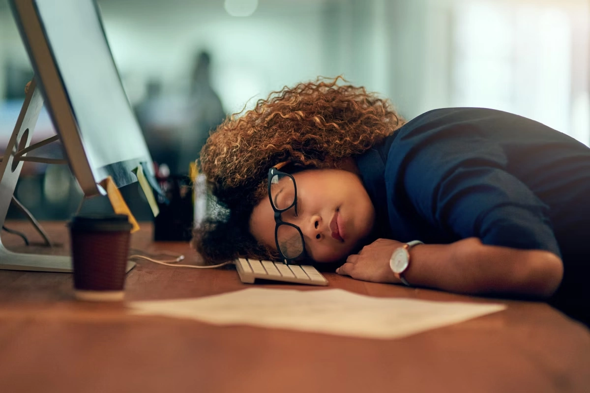 Mulher de óculos, com cabeça deitada em sua estação de trabalho