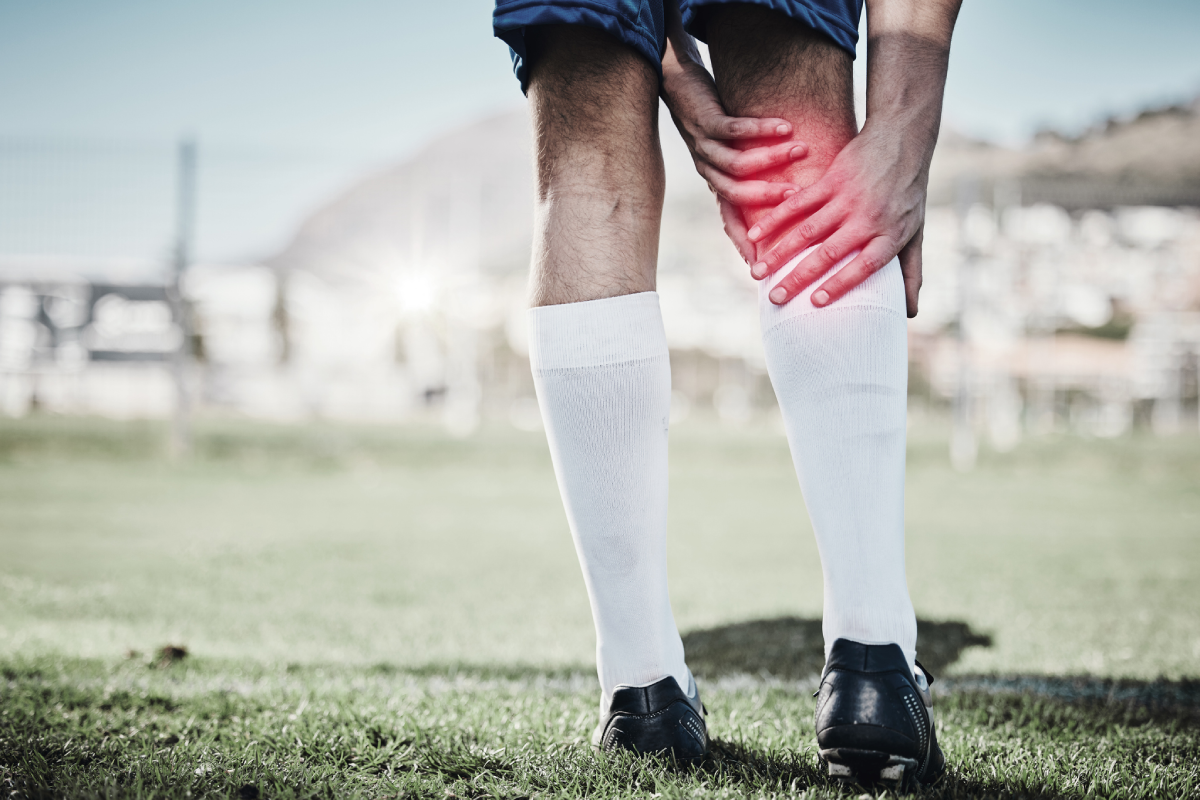 Detalhe de um jogador de futebol tocando a panturrilha em um local destacado por luz vermelha, representando o foco da dor