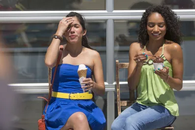 Uma mulher tomando sorvete e com a mão na cabeça com fisionomia de incomodo e outra tomando sorvete e sorrindo