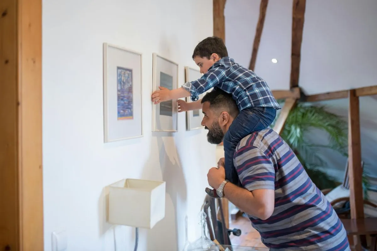 Homem carrega seu filho pequeno nos ombros dentro de casa, mostrando a importância de uma vida sem dores no pescoço para aproveitar os momentos em família.