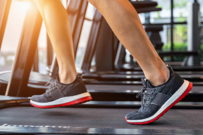 Detalhe de pés calçados com tênis de corrida, posicionados para um treino em esteira de academia.