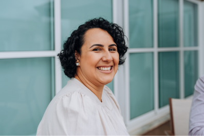 Mulher sentada, com mão na têmpora direita, no escritório, de olhos fechados.