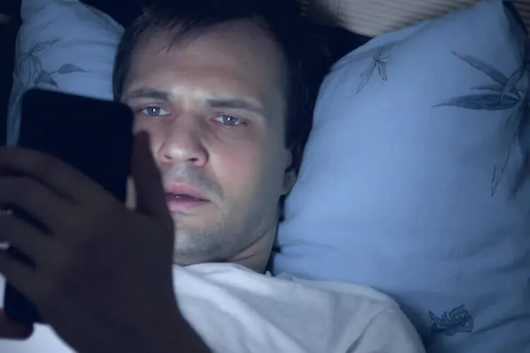 Homem ao celular deitado na cama
