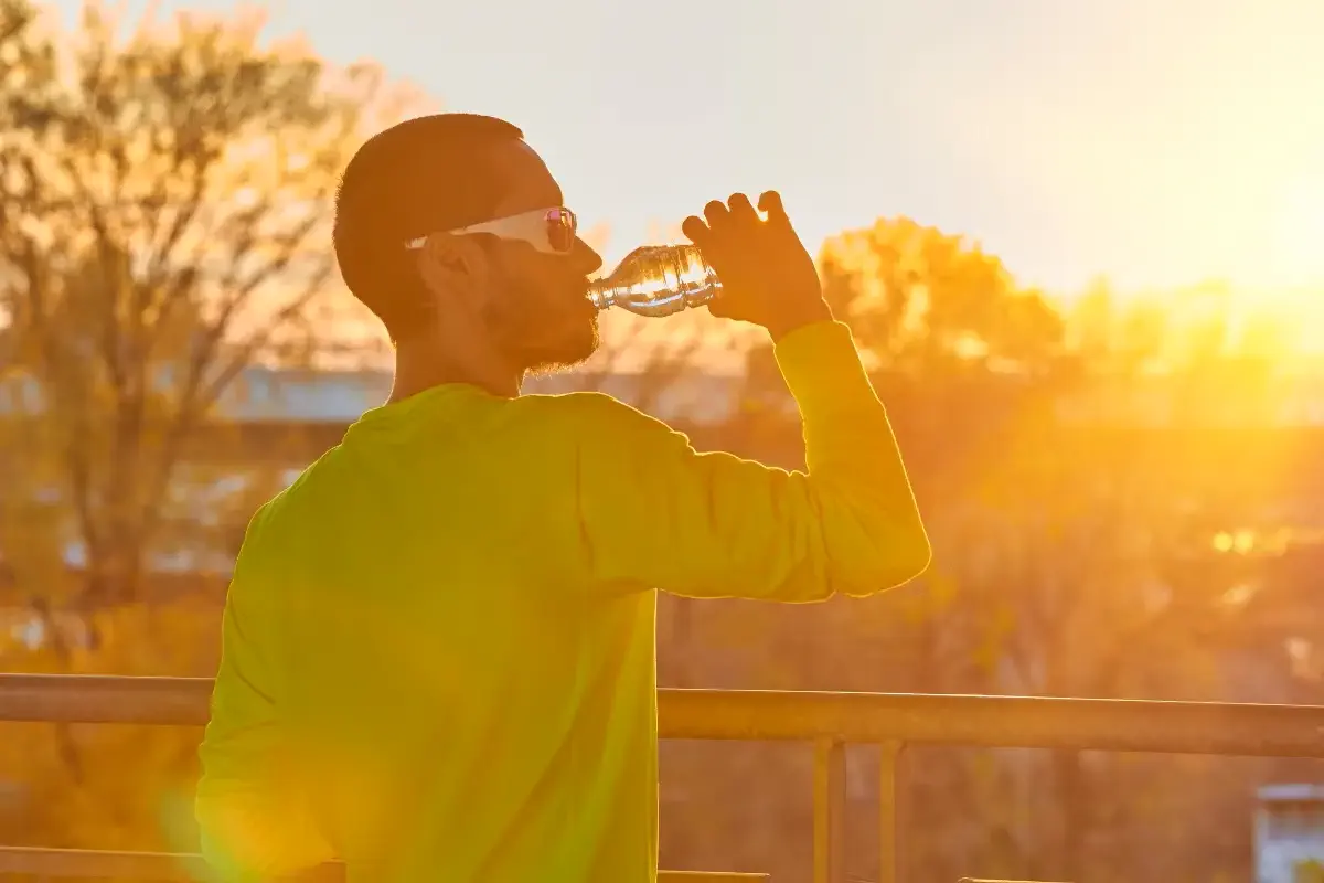 Homem exposto ao sol se hidratando, usando óculos escuro e com blusa que protege os braços