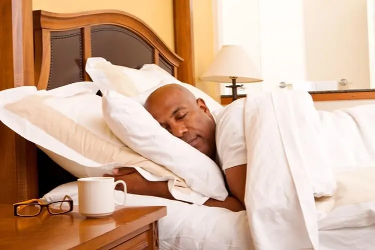Homem dormindo de lado na cama, coberto com edredom branco.